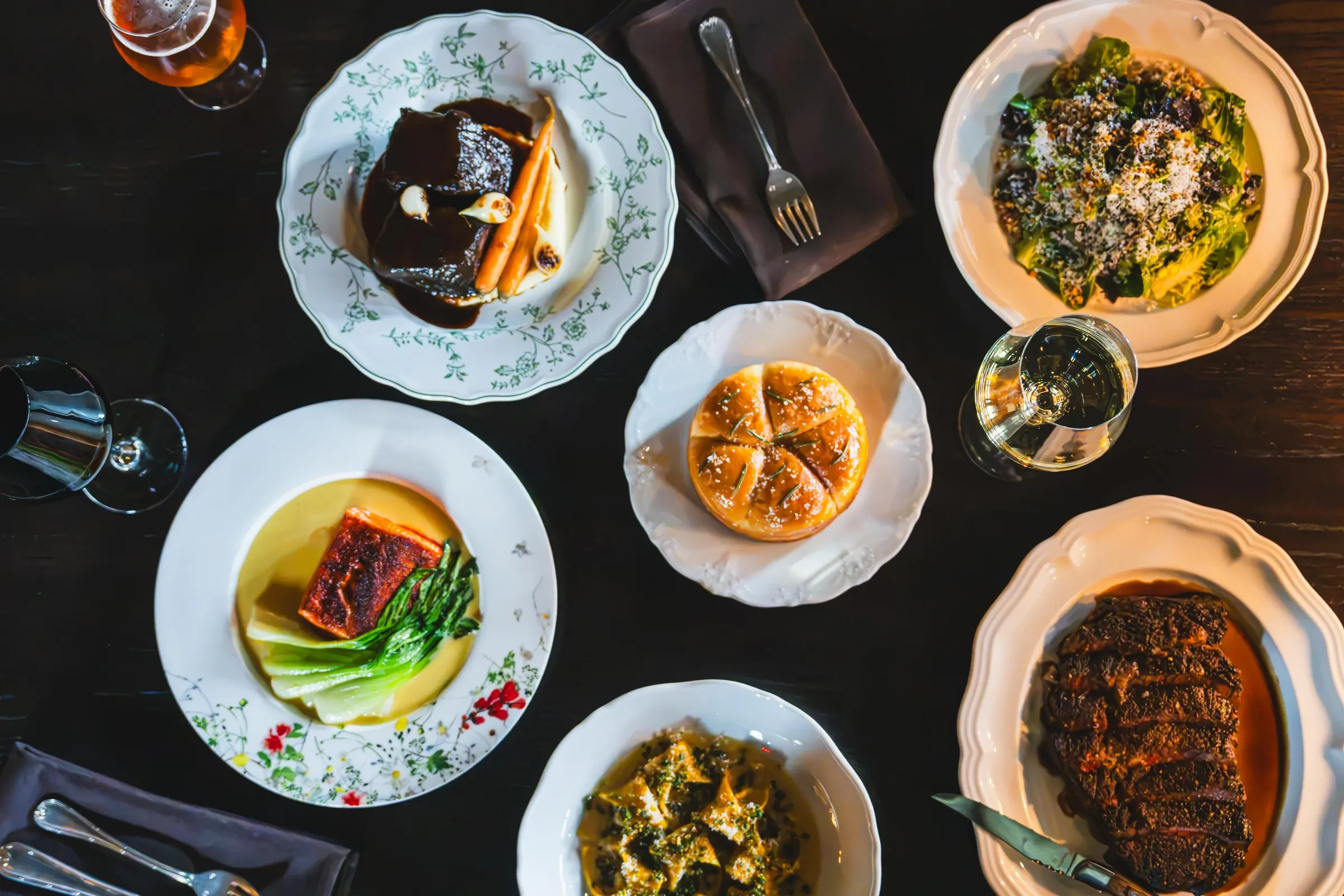 Dinner from above: short rib, salmon, a salad, bread, tortellini, and steak on patterned plates