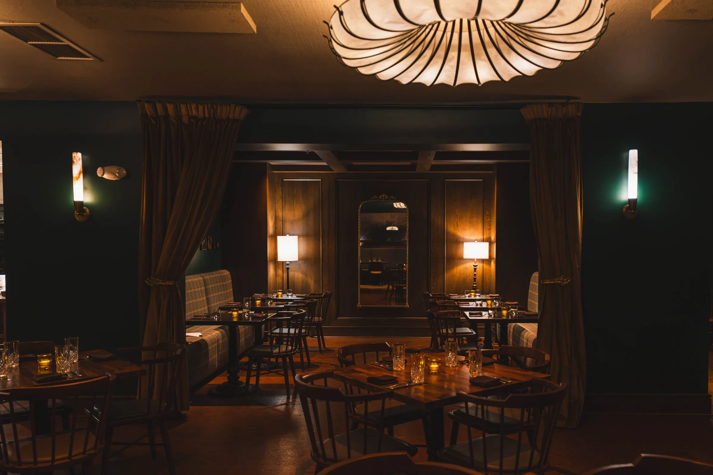 The Nook through open velvet curtains: plaid banquettes, table lamps, and a tall mirror