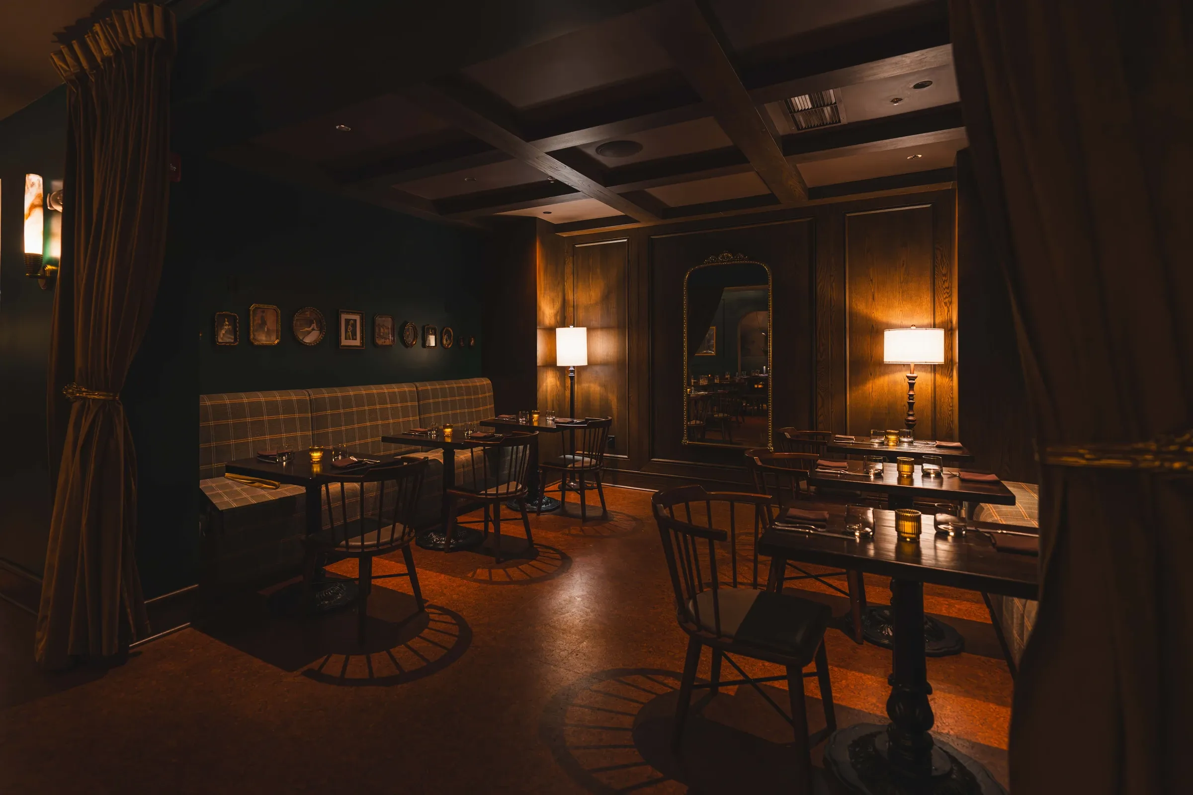 Tables in The Nook with candles, framed pictures on the dark green wall, curtains at each side
