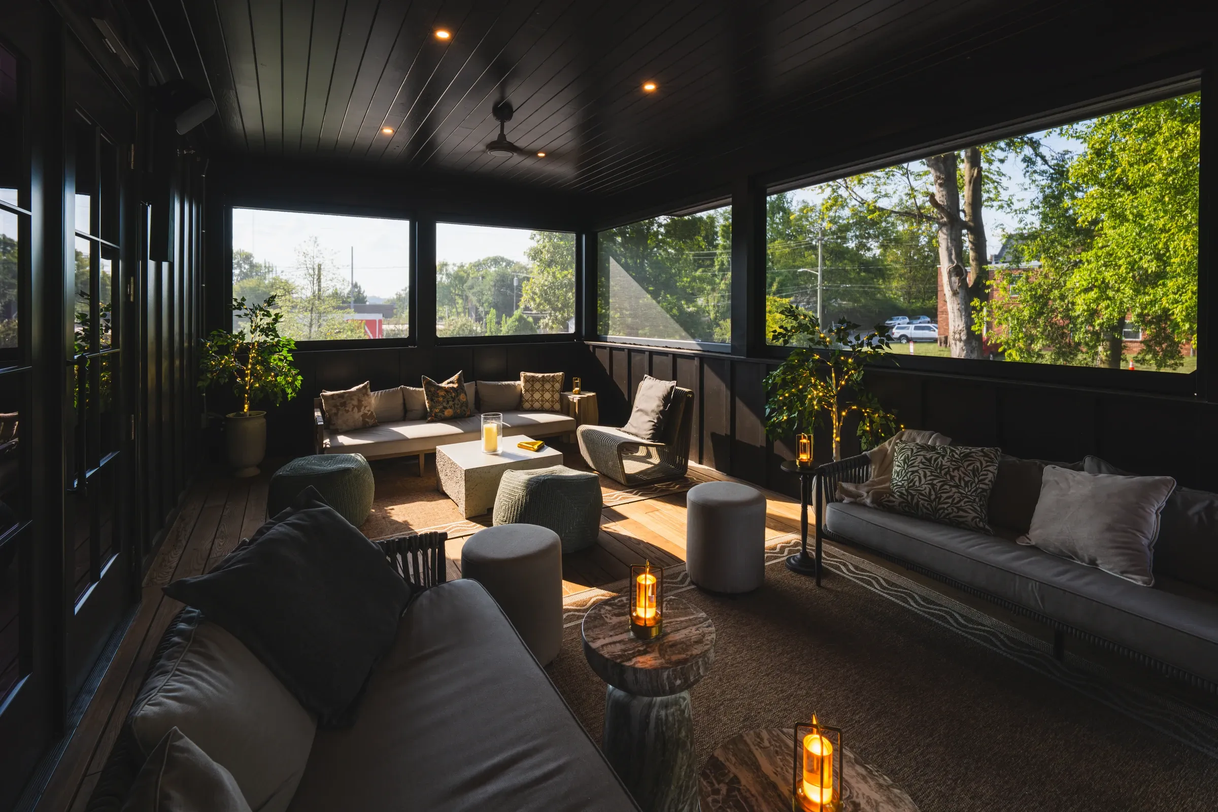 The covered upstairs terrace with sofas, low stools, and lanterns, trees outside the windows
